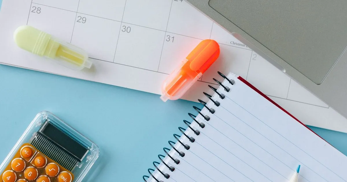 Wall calendar, highlighters, a calculator, and a notebook laid out on a blue desk
