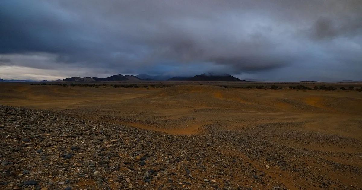 Dark storm clouds over a rocky desert plain with mountains in the distance