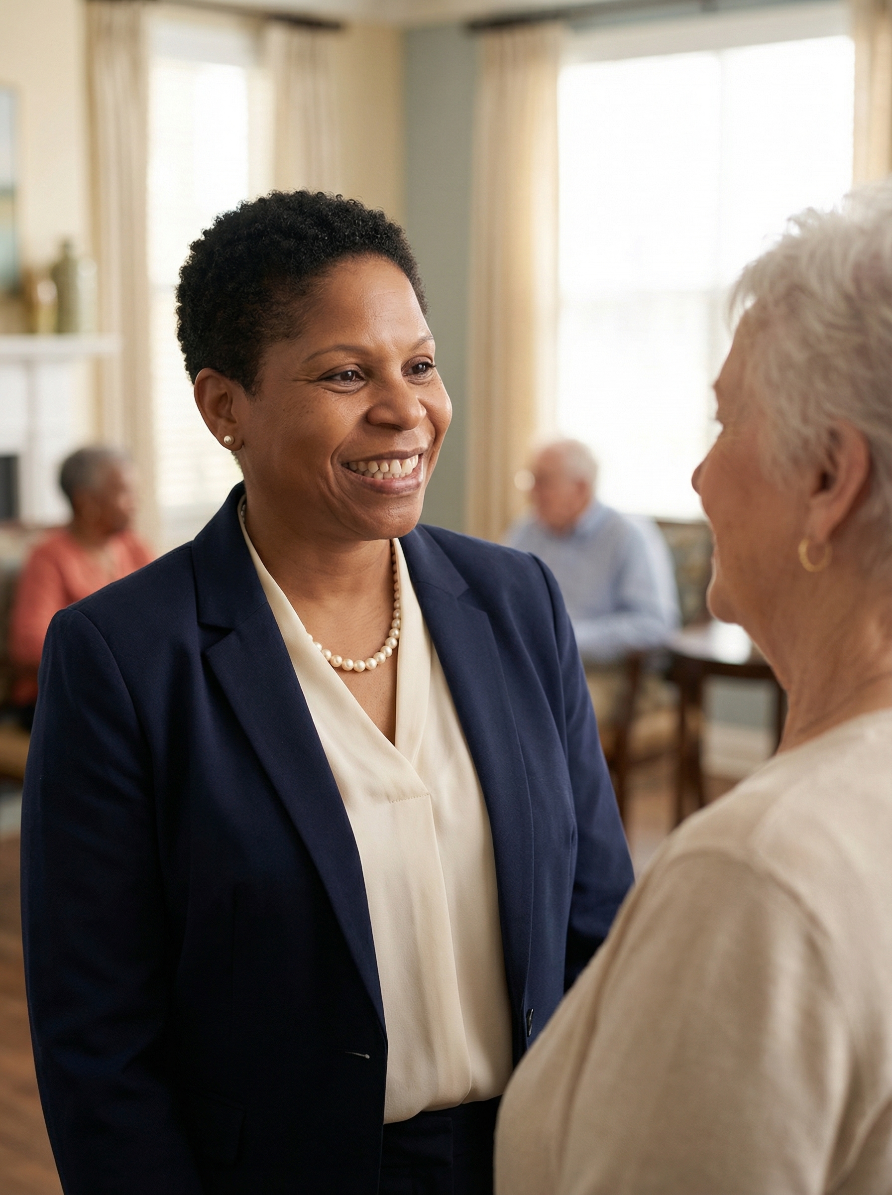 A young Latina caregiver with short hair, wearing a beige top, stands in a hallway holding a clipboard.