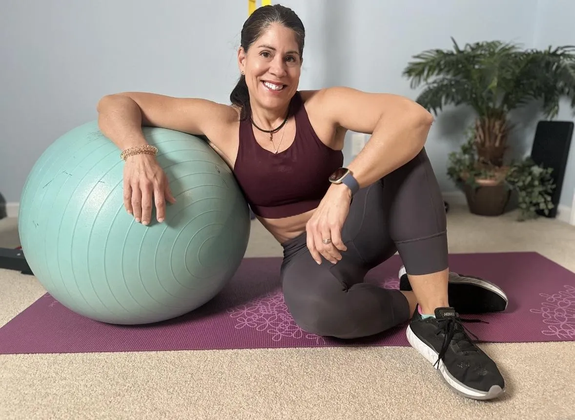 Olinda Branch smiling, sitting on a yoga mat at home and leaning on an exercise ball