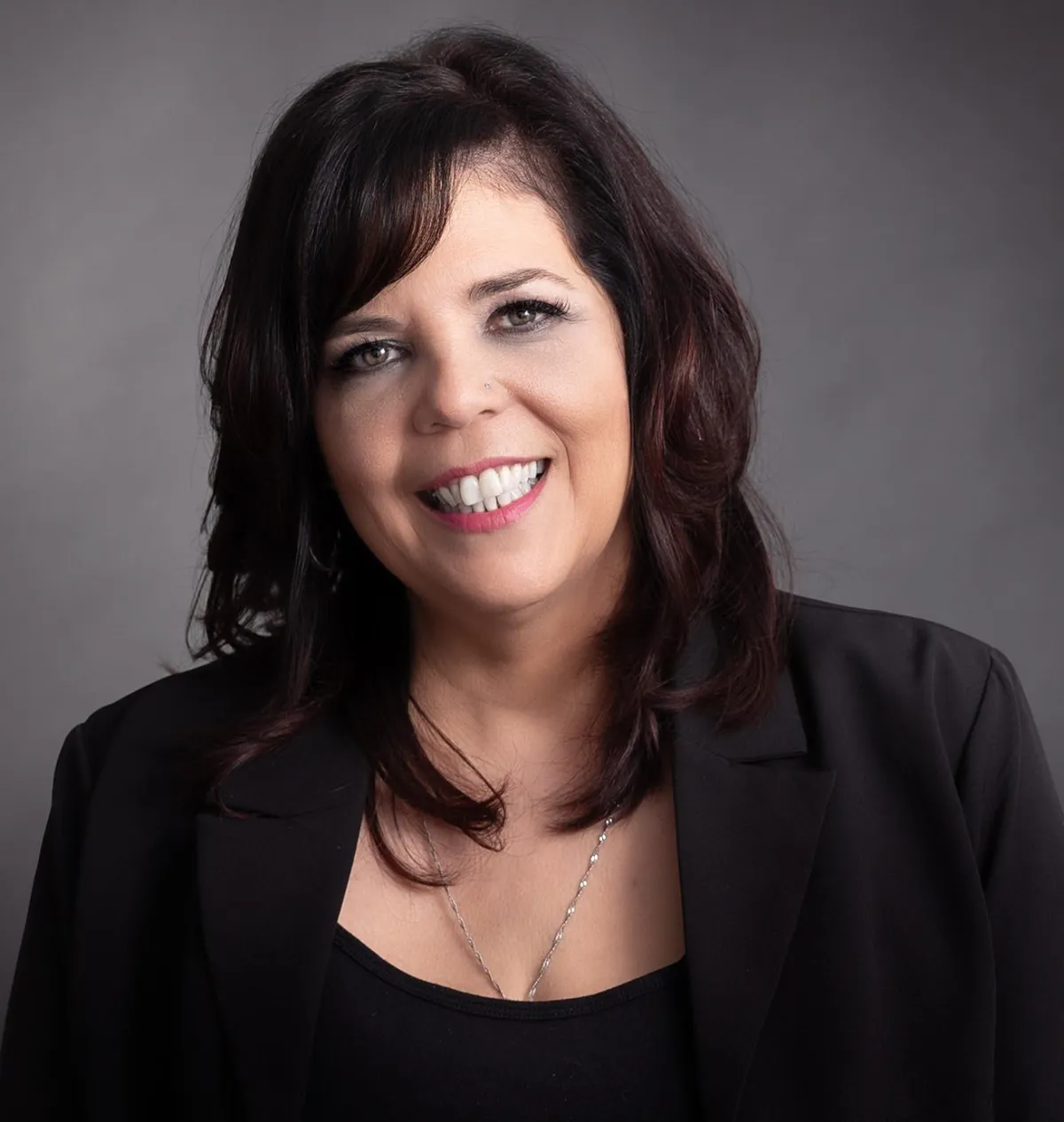 Robyn Bennett with dark shoulder-length hair, wearing a black blazer and necklace, smiling against a gray background.