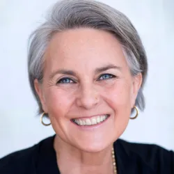 Kate Crow, mindset coach, smiling in a professional headshot with short gray hair and gold earrings.