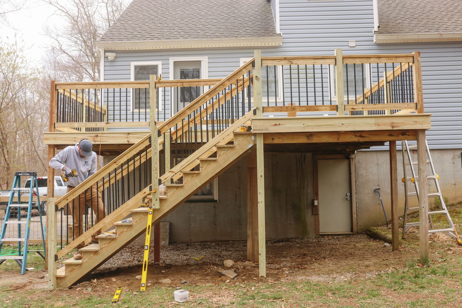 Crew member building pressure-treated wood deck stairs with black metal balusters