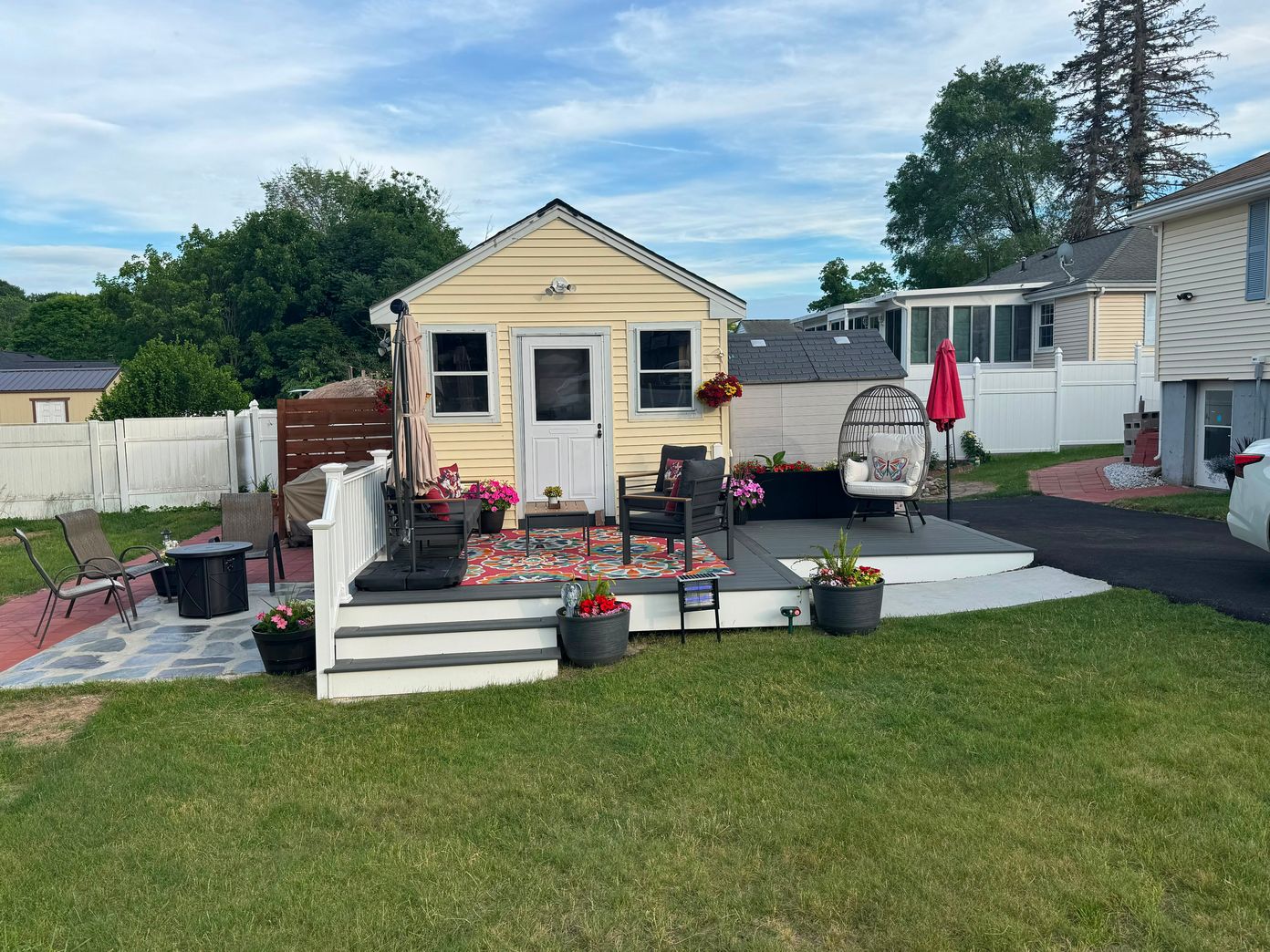 Gray composite deck with white railings and patio furniture beside a yellow cottage