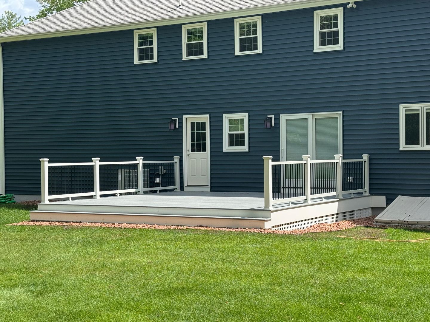 Low gray deck with white railings along a navy blue house