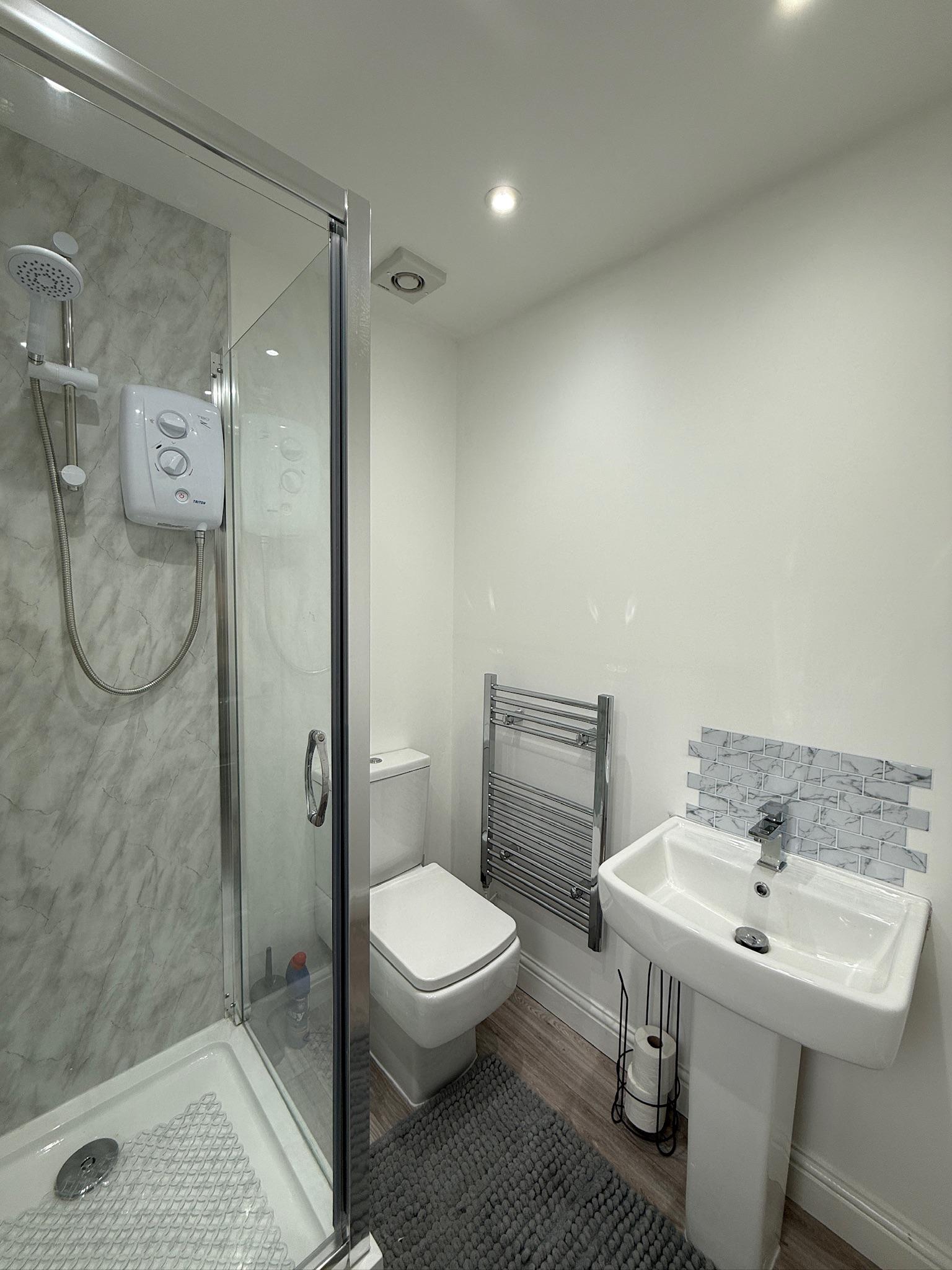 Modern garage conversion en suite bathroom with shower, toilet, sink and contemporary marble effect wall panels.