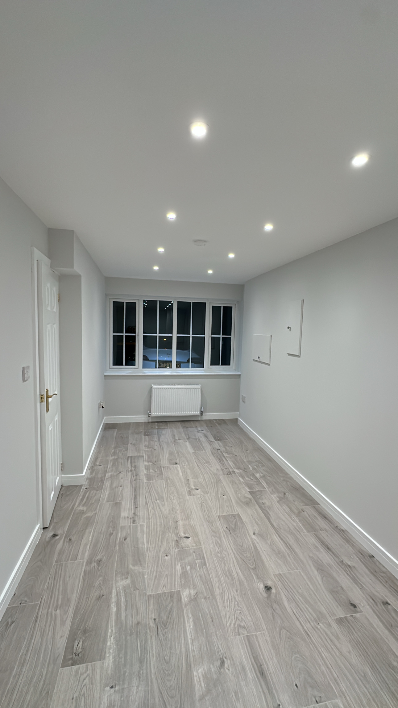 Modern single garage conversion with grey wood flooring, spotlights, radiator and bright contemporary finish.