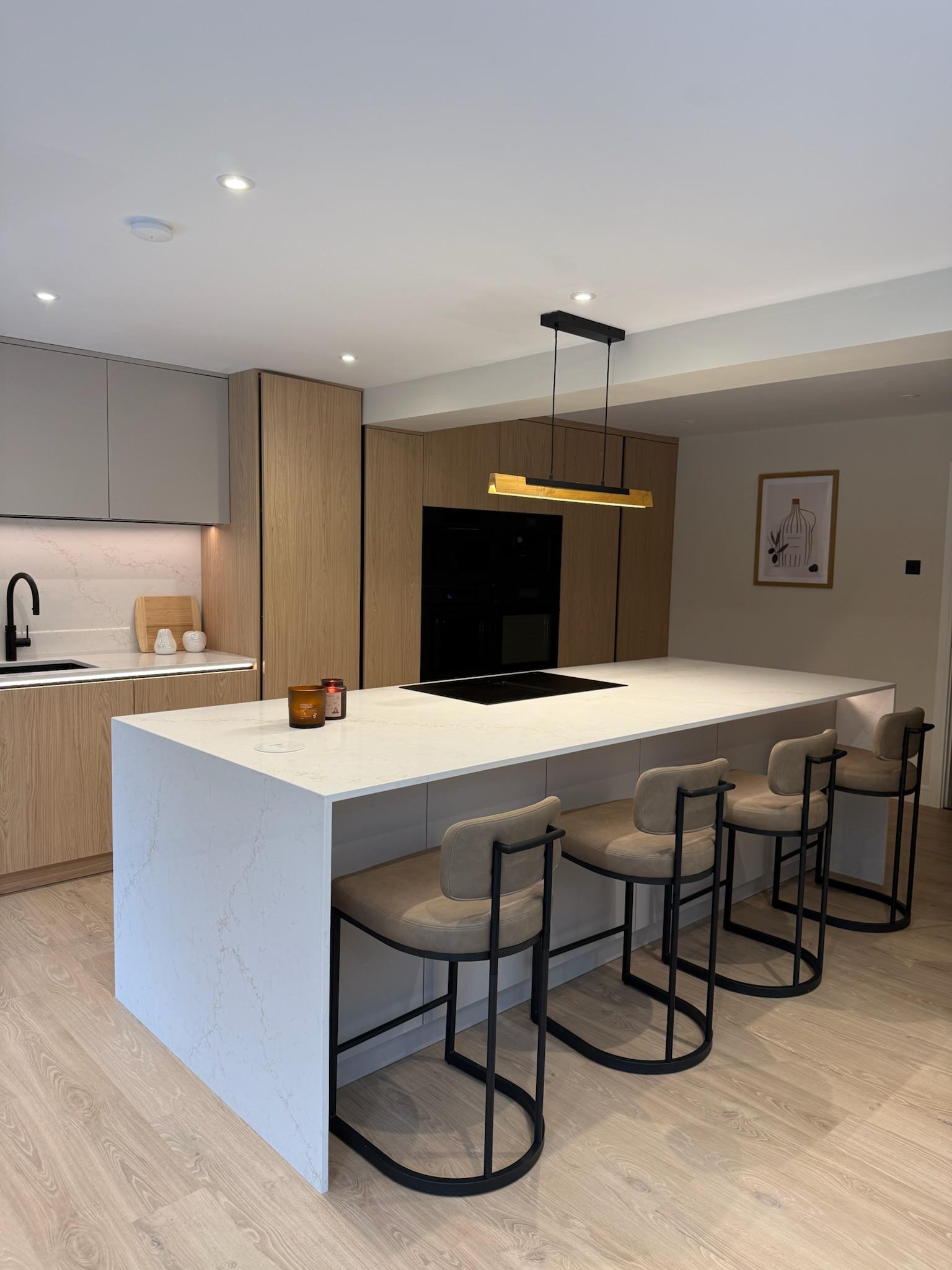 Modern open plan kitchen extension featuring a large quartz island, oak cabinetry, integrated appliances and contemporary pendant lighting.