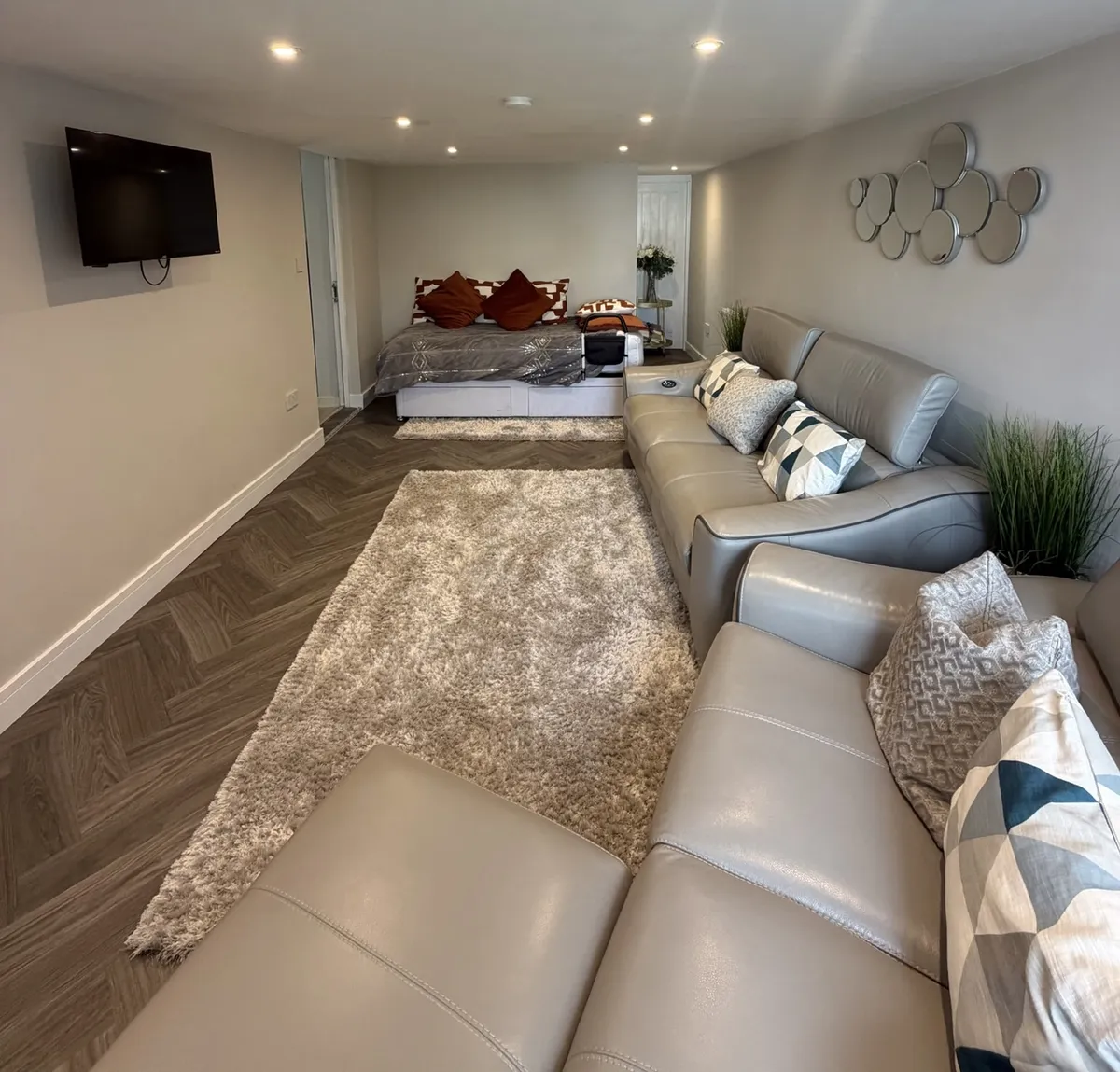 Garage conversion in Liverpool transformed into an annexe with bedroom and living area, featuring sofas, a bed, wall-mounted TV and herringbone flooring.