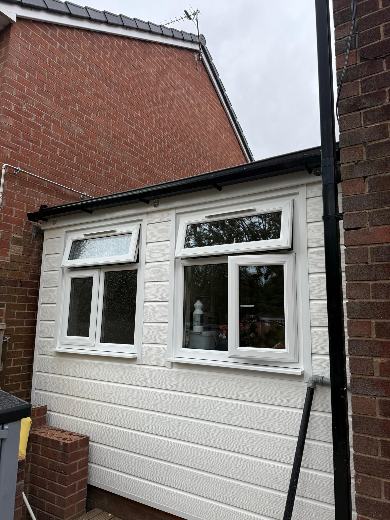 Exterior of an attached single garage conversion in Oldham, finished with new windows and white exterior cladding to create a second living room.