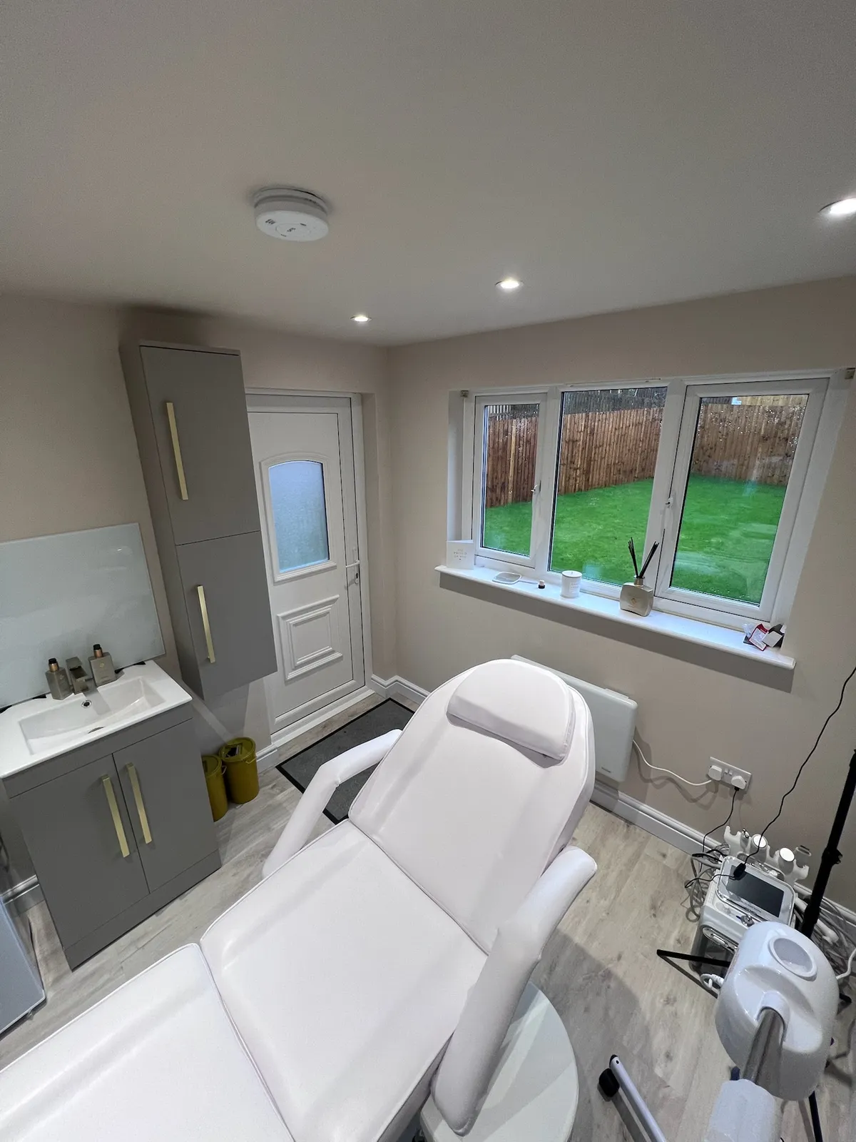 Single garage conversion in Rochdale transformed into a modern beauty salon with a treatment bed, professional beauty equipment, ceiling spotlights and large arched mirror.
