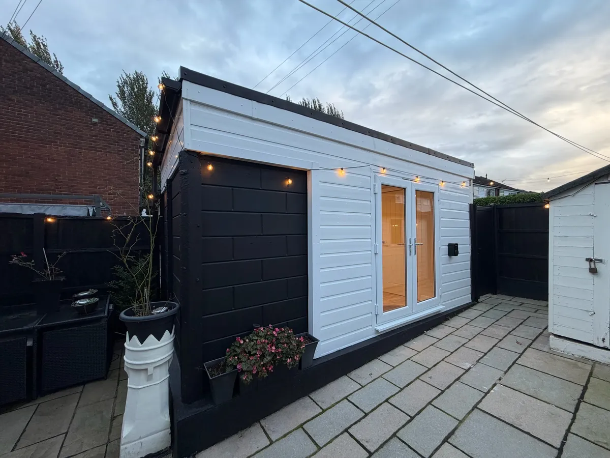 Single garage conversion in Bury transformed into a home office with storage, featuring white exterior cladding, black detailing and glazed French doors.