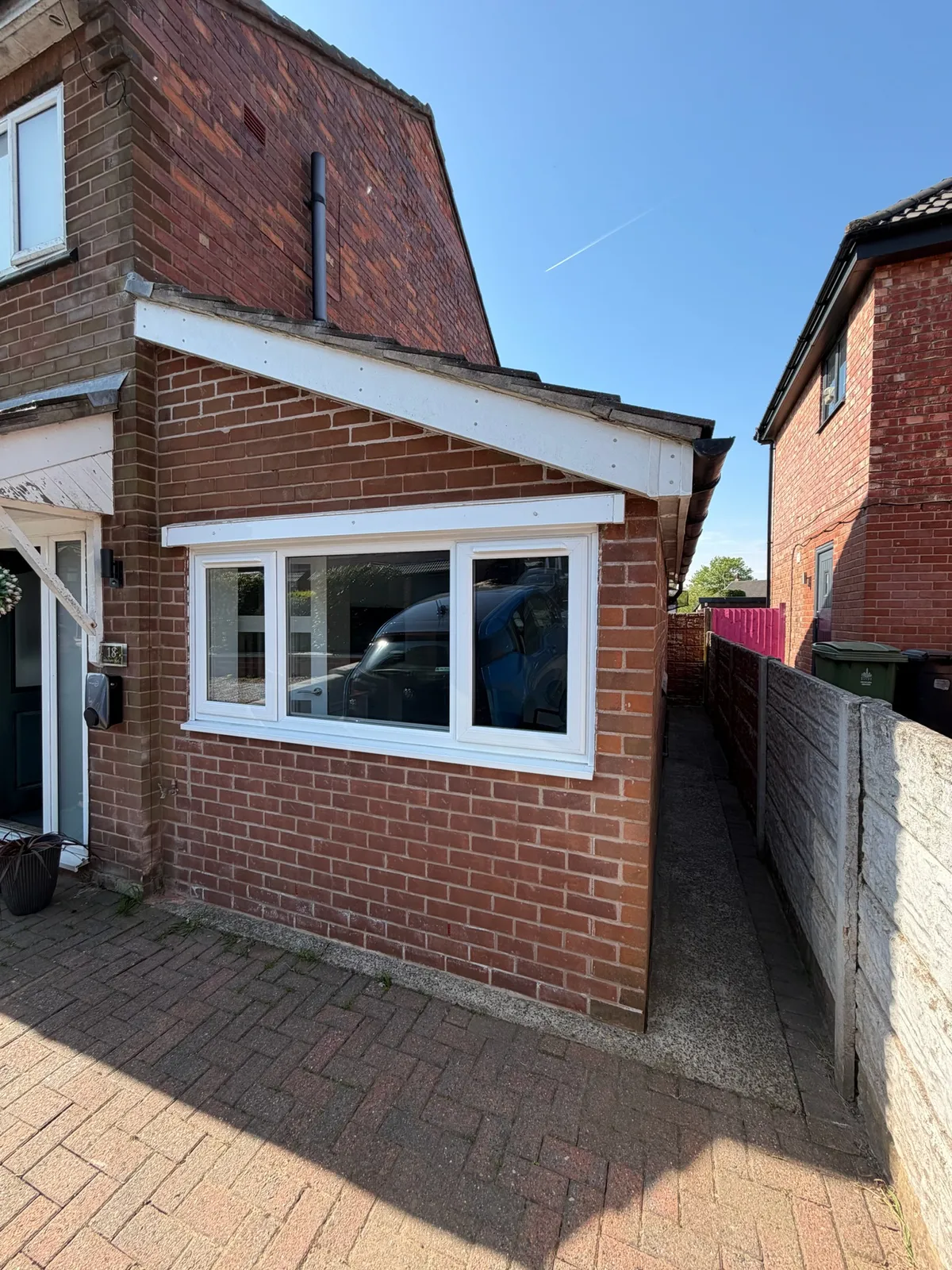 Exterior of a garage conversion in Stockport transformed into a second living room, featuring new brickwork, a large white-framed window and a pitched roof.