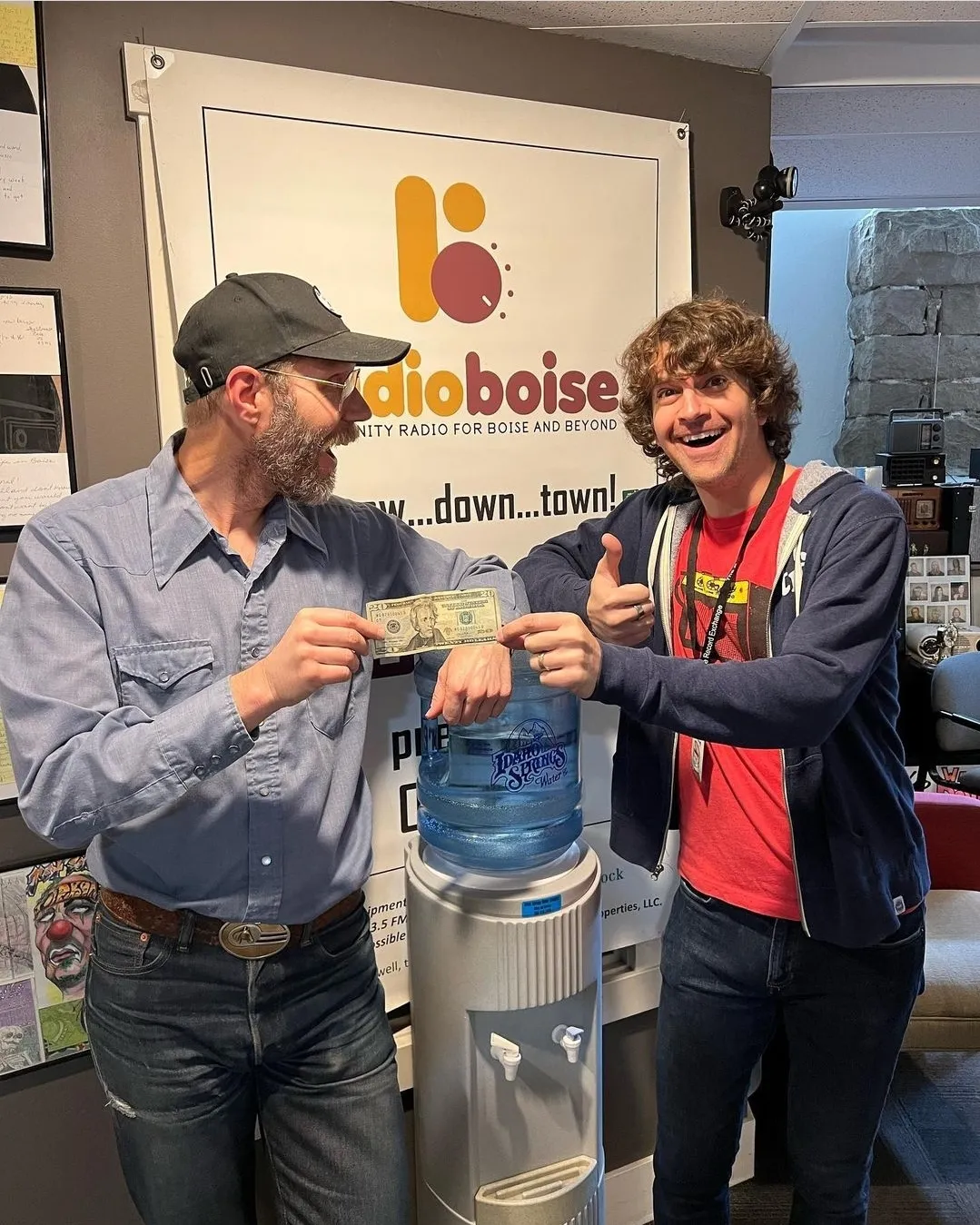 two guys smiling and holding a $20 bill by water station