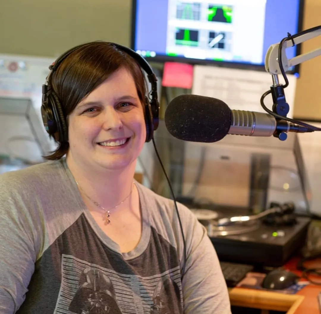 woman smiling and sitting by a microphone in a radio studio