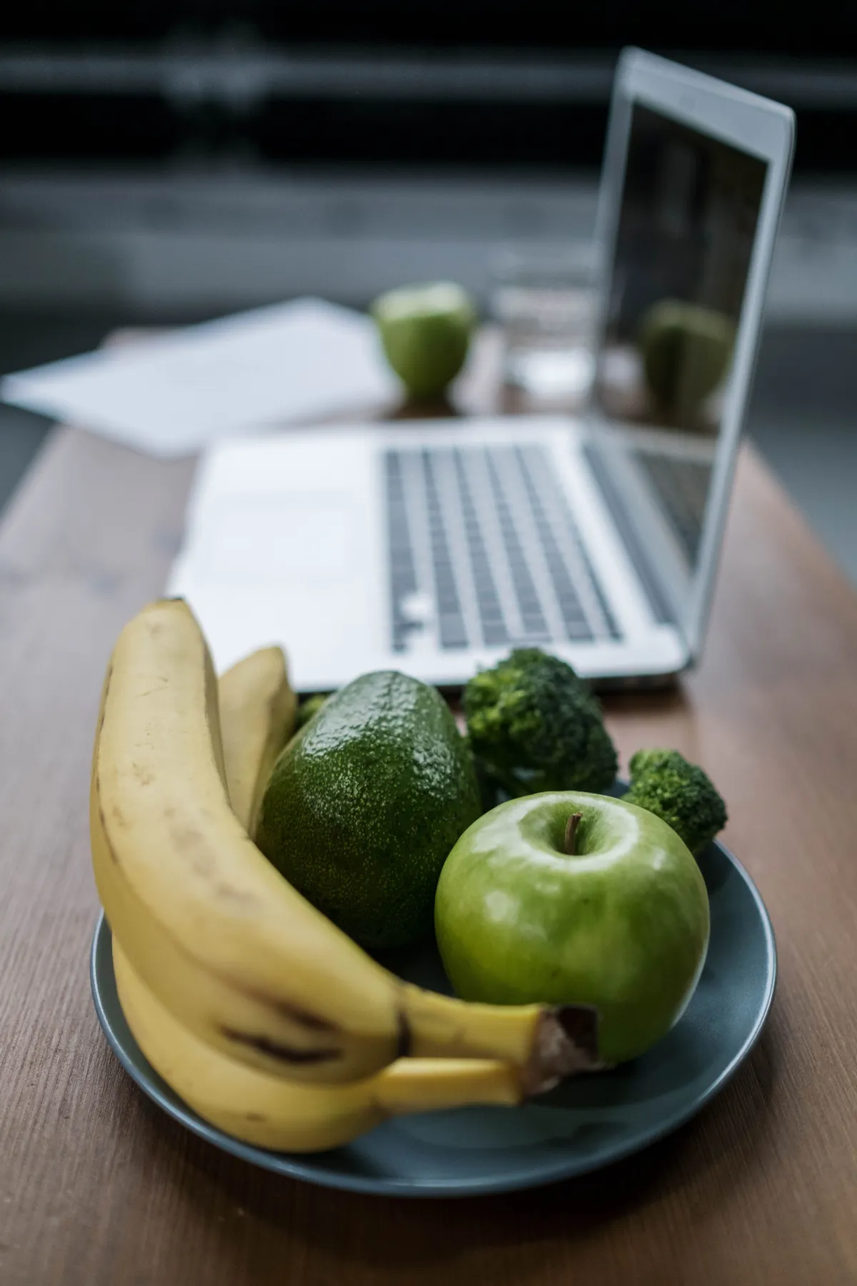 Healthy fruit bowl with bananas and green apples beside a laptop, practical nutrition advice
