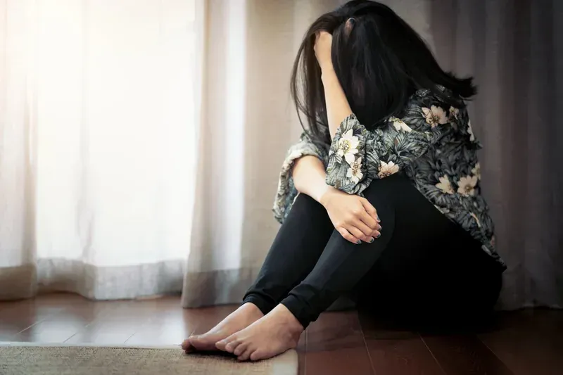Woman sitting on floor bent over with head down experiencing symptoms of depression — compassionate depression treatment available at Medivira in Frisco TX