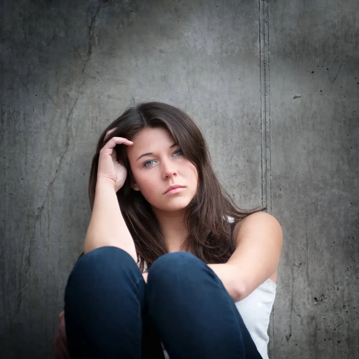 Young woman sitting against a concrete wall looking withdrawn and fatigued, illustrating symptoms of dysthymia (persistent depressive disorder) — Medivira