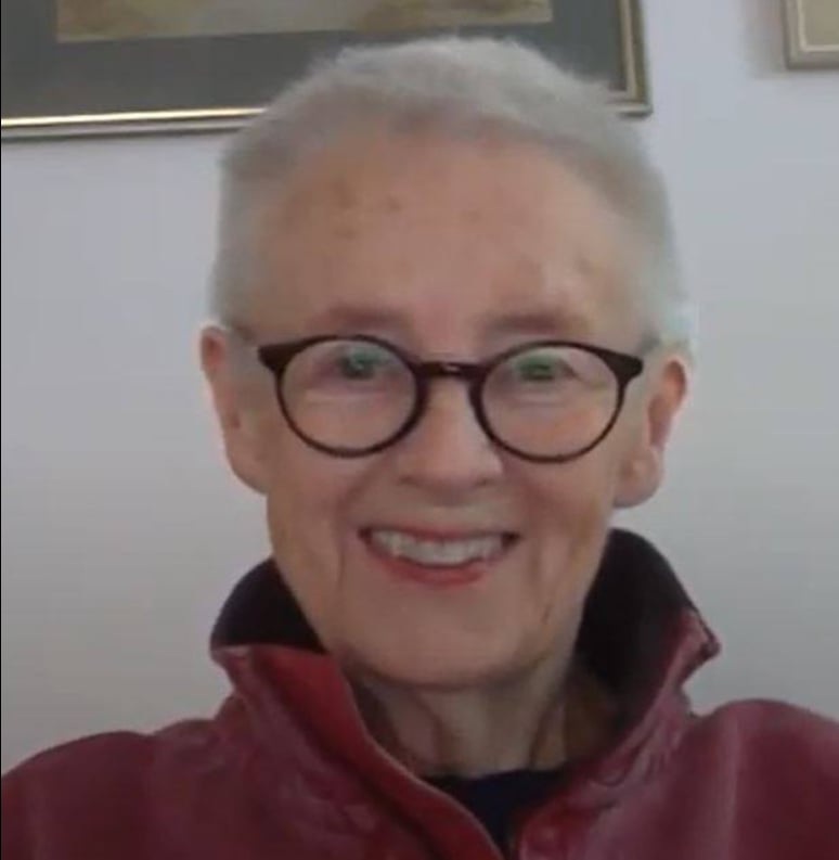 A smiling woman in her 30s, holding a notepad, with a border collie at her side, standing in a sunlit home office. The setting is cozy and professional, reflecting her role as a canine behaviourist.