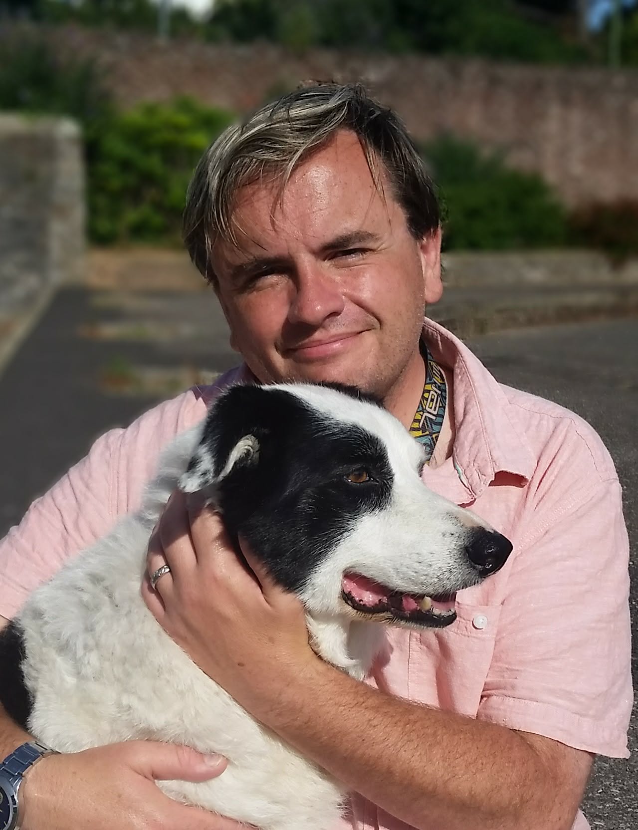 A smiling woman in her 30s, holding a notepad, with a border collie at her side, standing in a sunlit home office. The setting is cozy and professional, reflecting her role as a canine behaviourist.