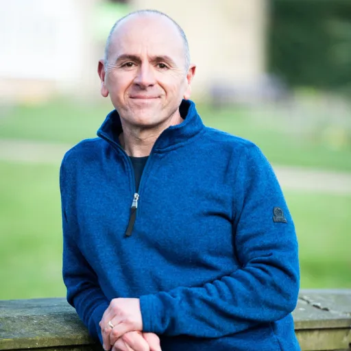 A photo of Tony smiling and leaning against a stone wall