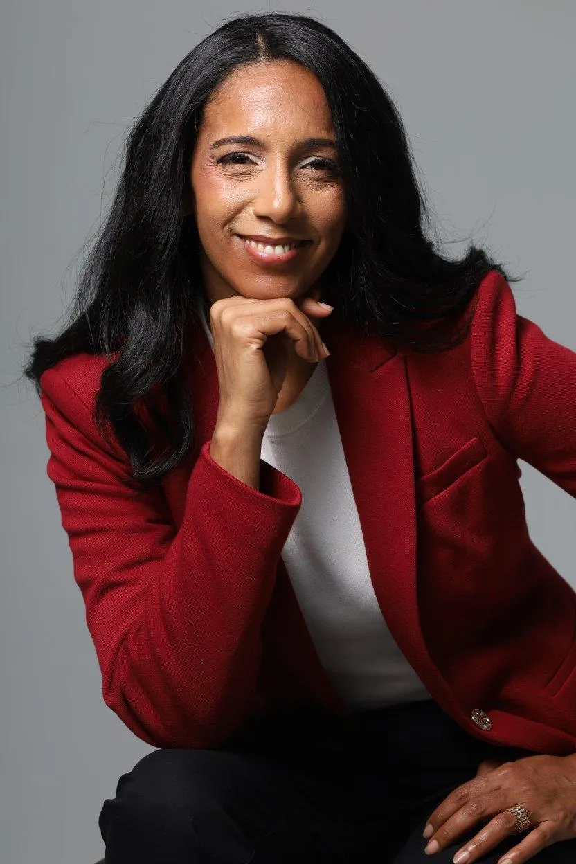Professional portrait of a woman in a red blazer, smiling confidently with her hand under her chin, representing NSantos Consulting on a contact page for client inquiries and consultations.