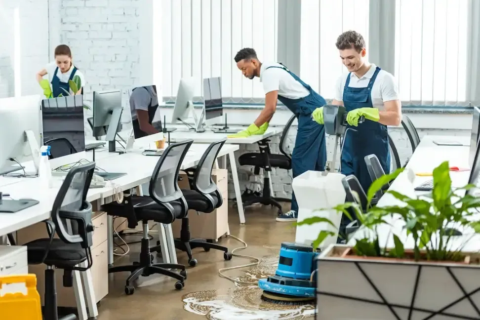 A group from TuClean Commercial cleaning service team in professional cleaning uniforms waxing an office floor and wiping office tablesng the floor and cleaning the office desks