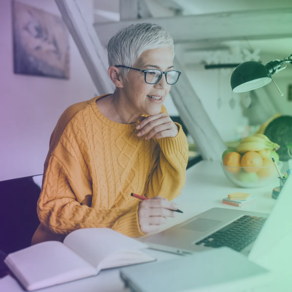 Lady over 50 in a yellow jumper working on her laptop at a desk