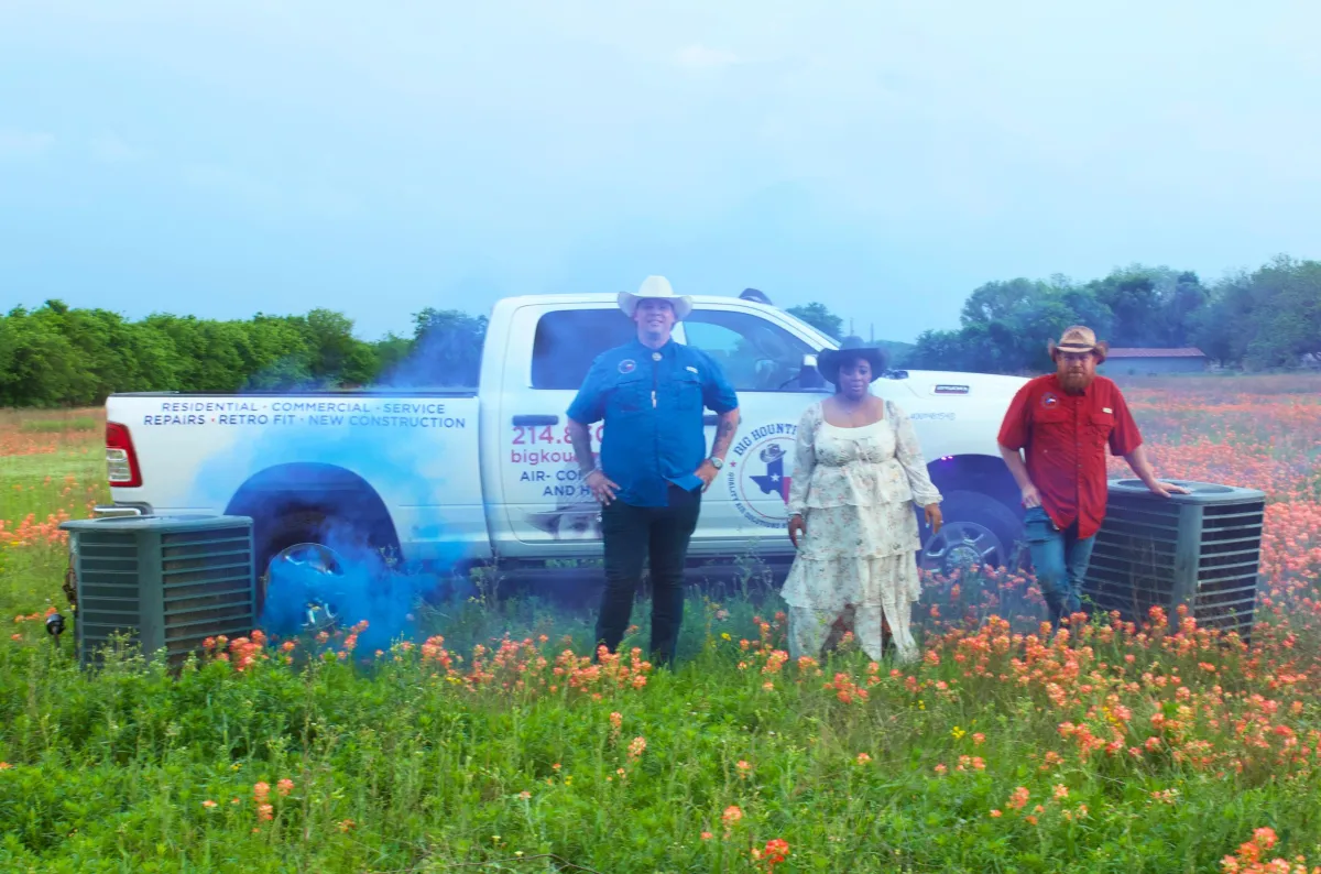 HVAC repair and installation team in Texas standing by service truck and air conditioning units in a field of wildflowers, representing local heating and cooling services.