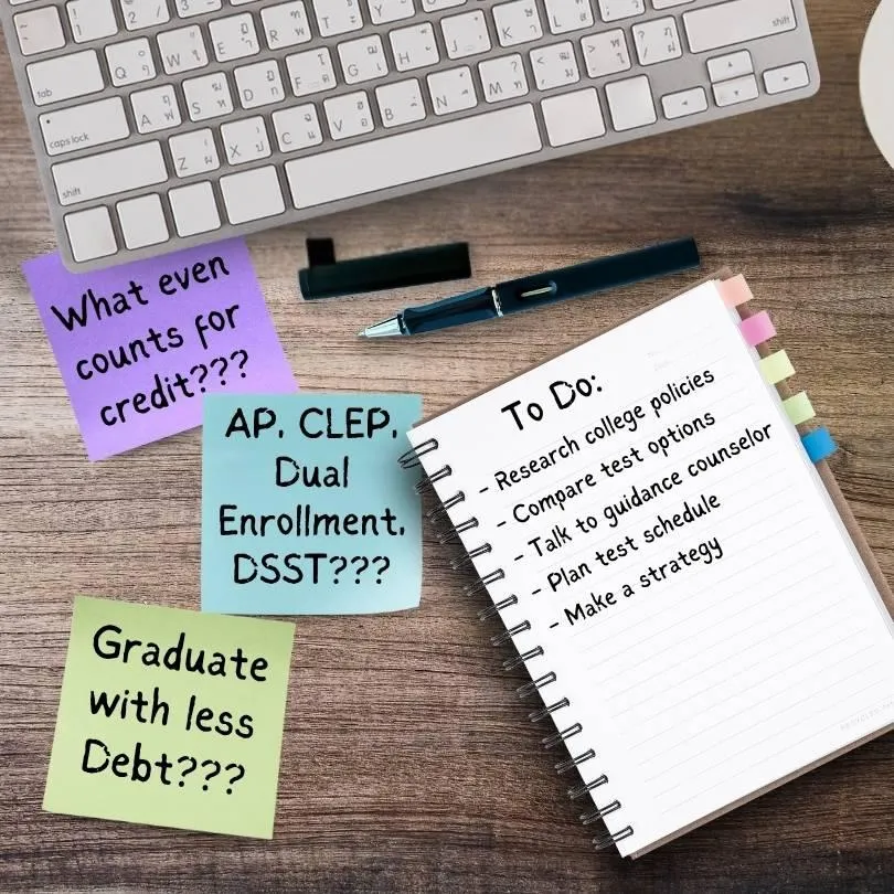 Flat lay of a wooden desk with a white keyboard, pen, and spiral notebook labeled 'To Do' listing steps for college credit planning. Sticky notes around the notebook read: 'What even counts for credit???', 'AP, CLEP, Dual Enrollment, DSST???', and 'Graduate with less Debt???'. Visual represents a parent’s overwhelmed mindset while researching college credit options for their teen.