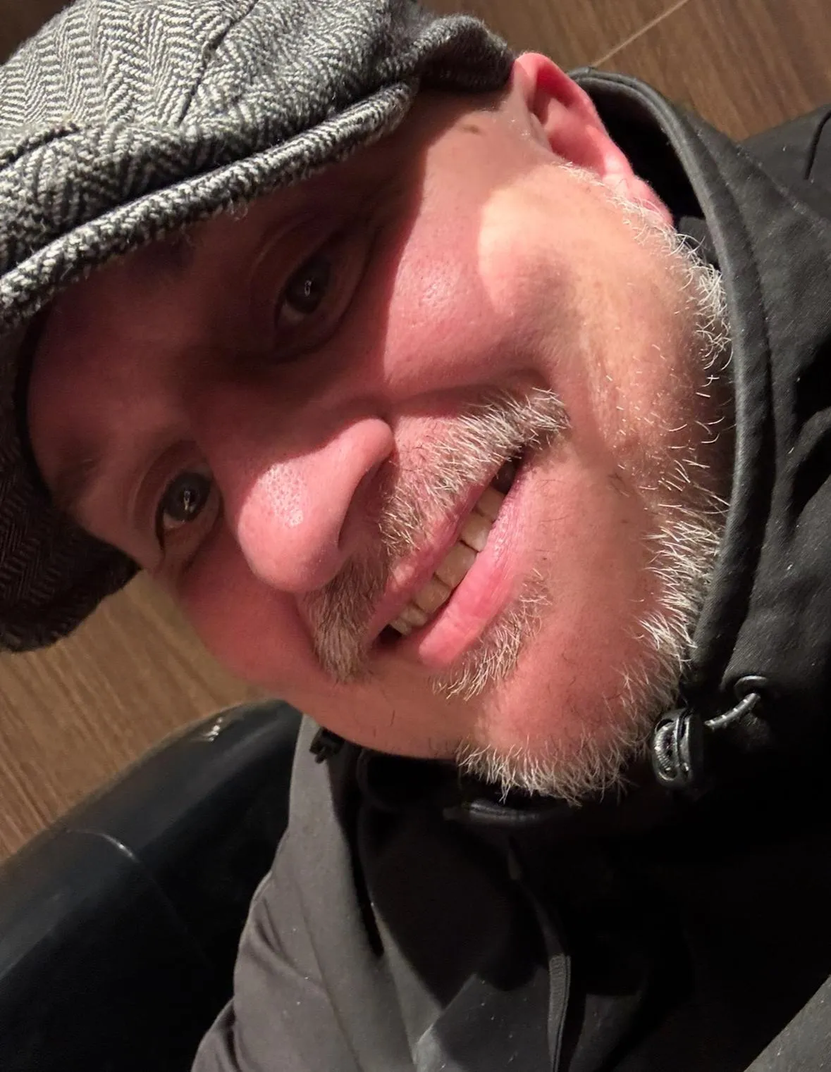 Portrait of a smiling middle-aged woman with short brown hair, wearing a blue blouse, standing in a bright, welcoming office with community posters in the background.