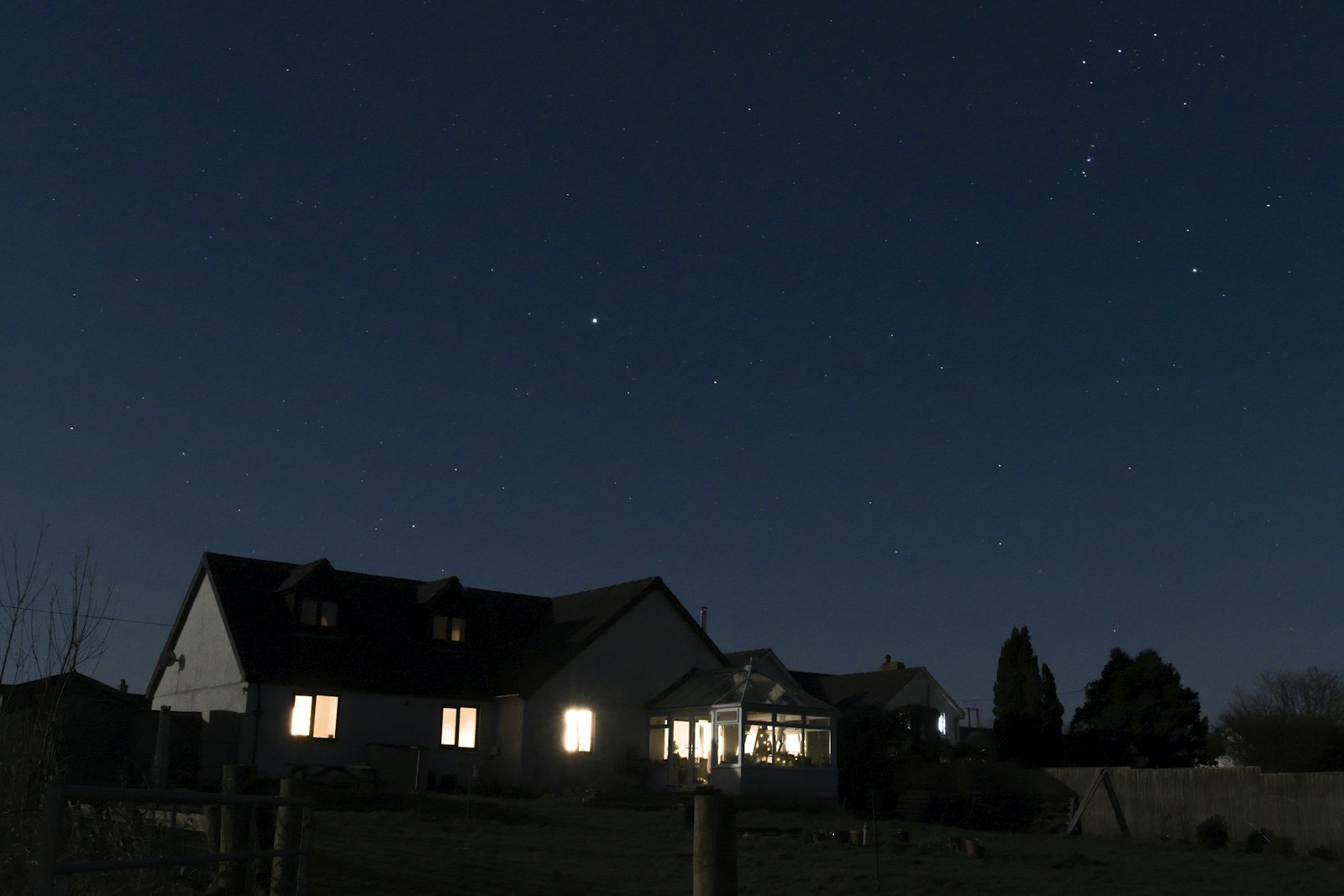 Single-story home glowing with warm lit windows at night under a clear starry sky