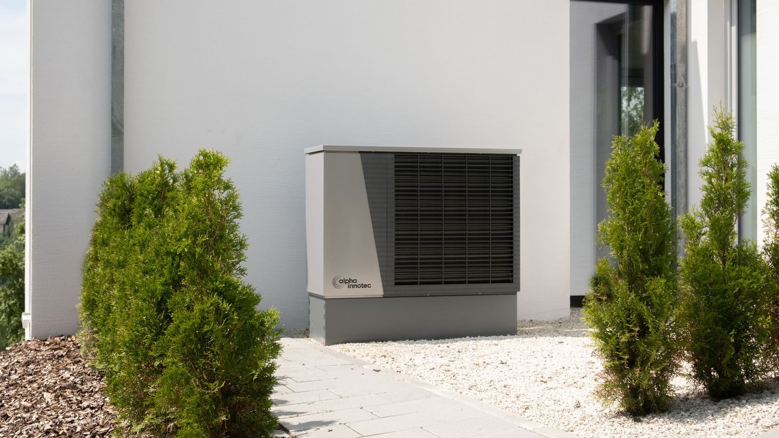 Residential heat pump outdoor unit installed beside a modern white home with landscaping