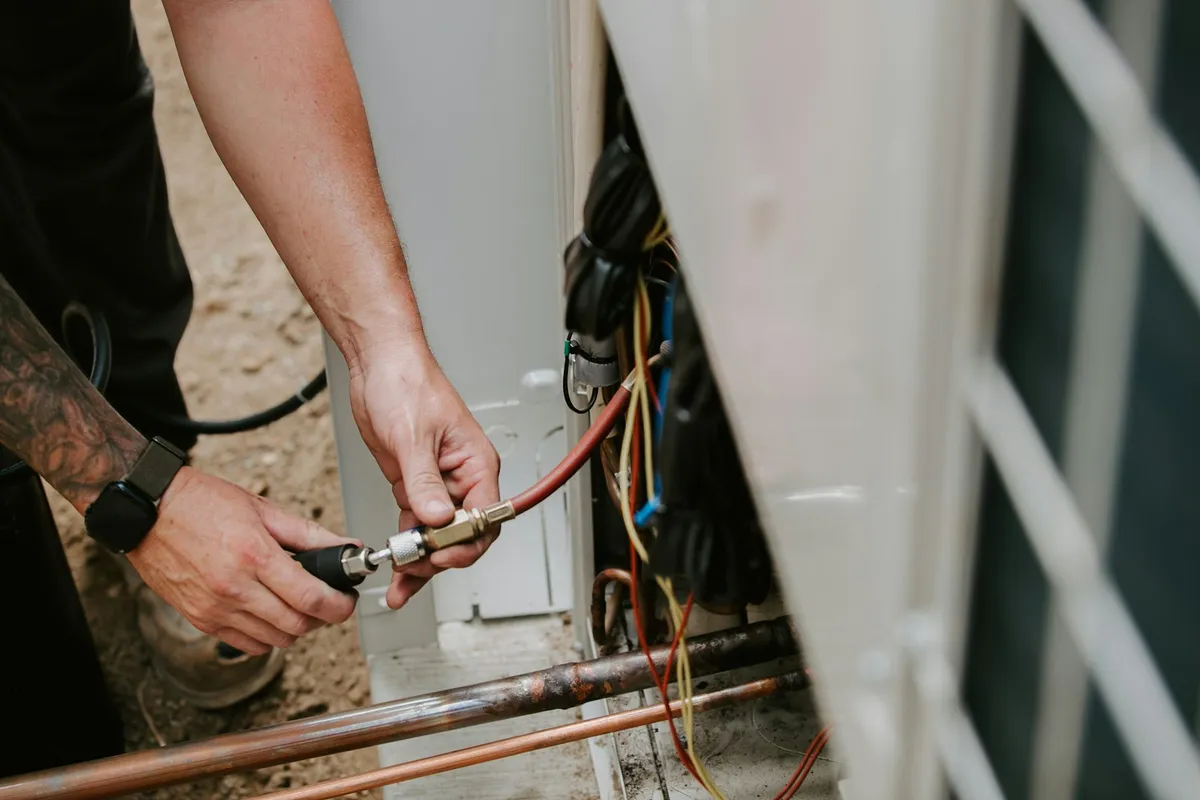 HVAC technician connecting a refrigerant pressure gauge to an outdoor AC unit's electrical and line set during a maintenance visit in Cape Coral