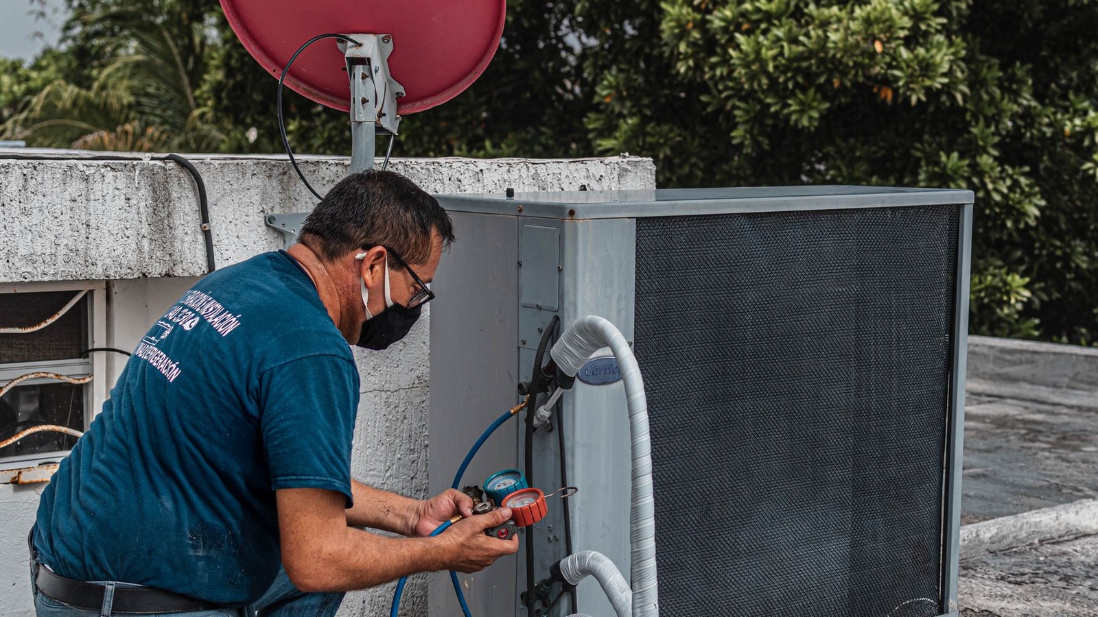 HVAC technician using manifold gauges to service an outdoor condenser unit on a Florida rooftop