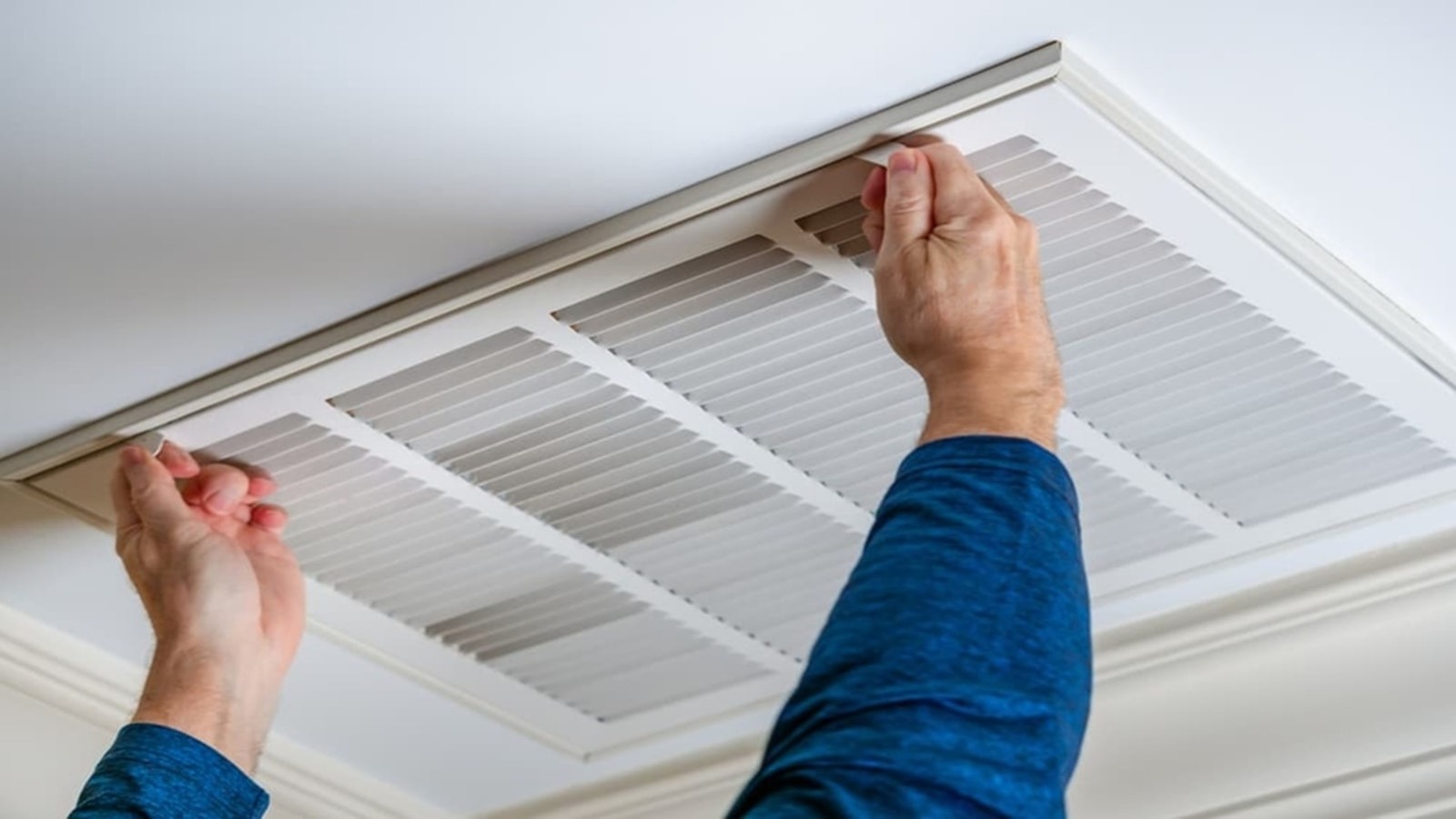 A homeowner opening a ceiling return air grille to reach the air filter inside