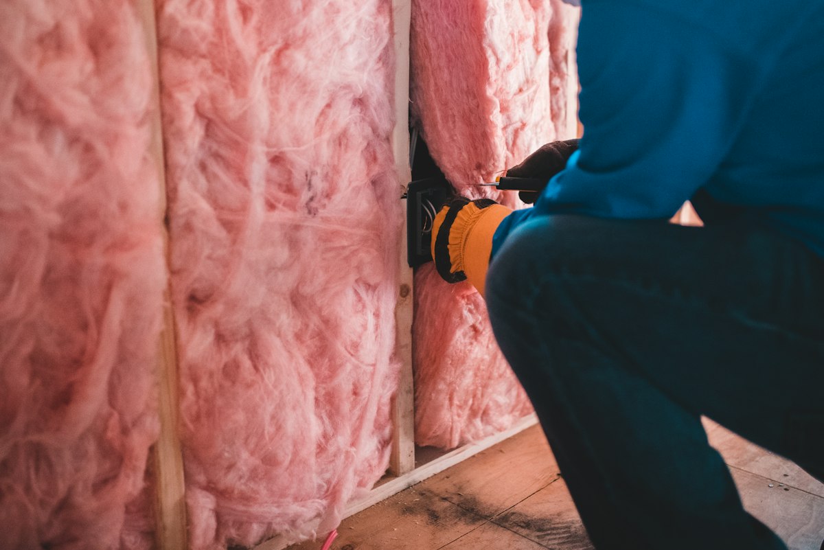 Technician installing pink fiberglass insulation between wall studs