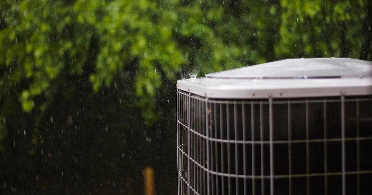 Outdoor residential air conditioner condenser unit in a Cape Coral backyard during a rainstorm