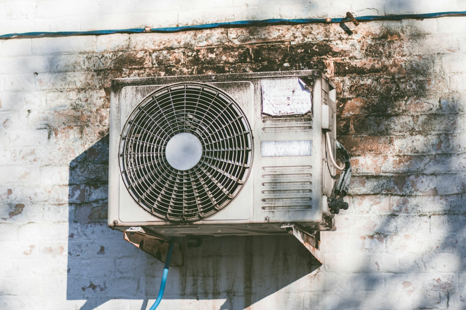 Old, rust-streaked outdoor air conditioning unit mounted on a weathered wall, showing the wear of a system nearing the end of its life