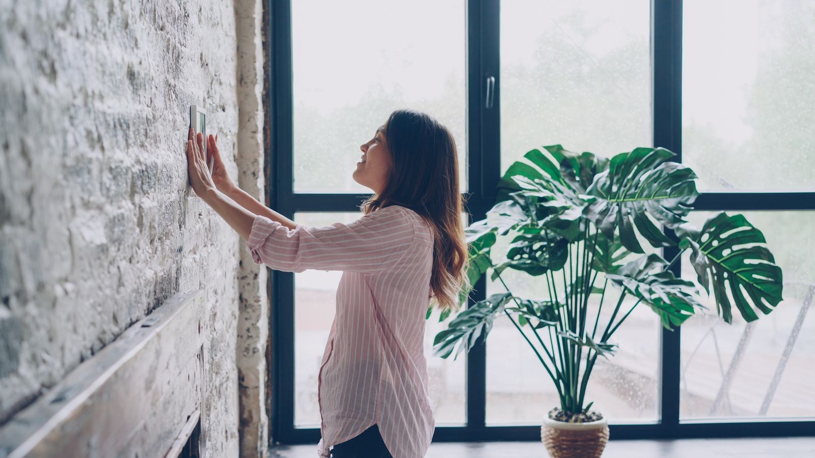 Homeowner adjusting a wall-mounted thermostat in a bright living room