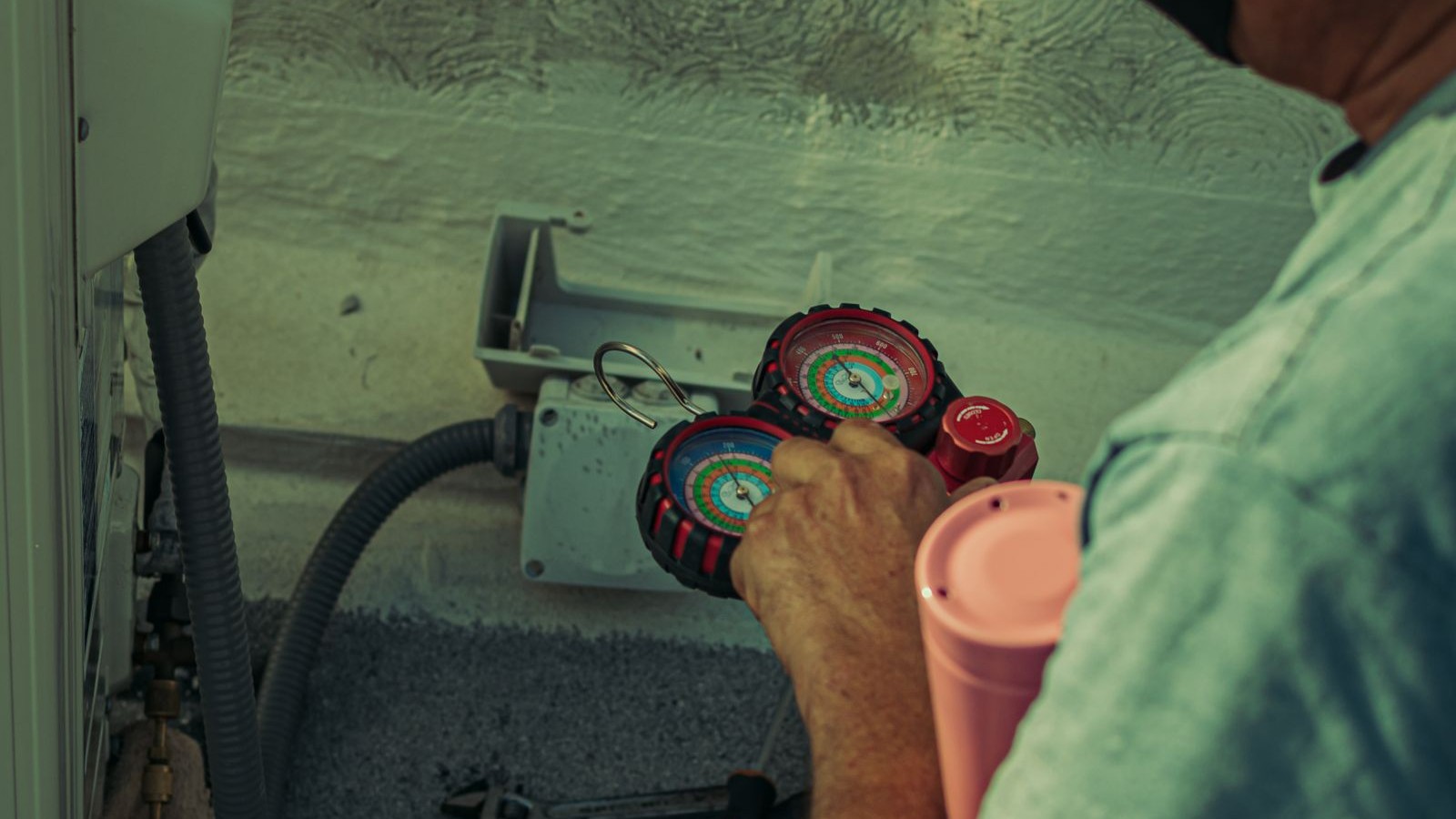 HVAC technician checking refrigerant charge on an outdoor air conditioning unit with manifold gauges