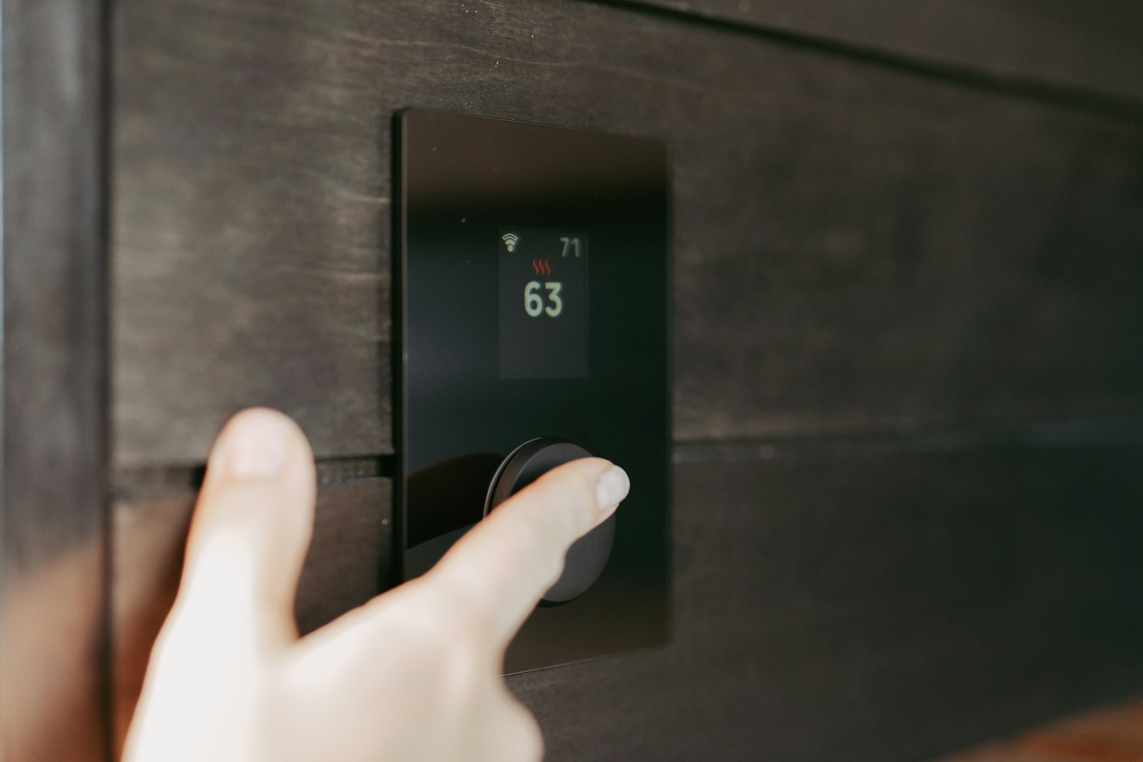 Hand adjusting a modern digital wall thermostat