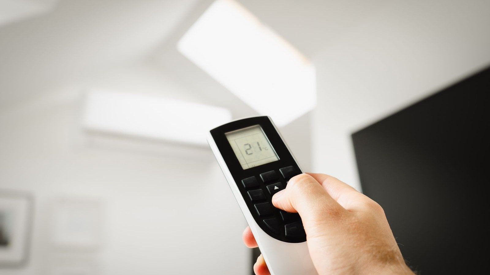 Homeowner pointing a remote at a wall-mounted air conditioner in a Florida living room