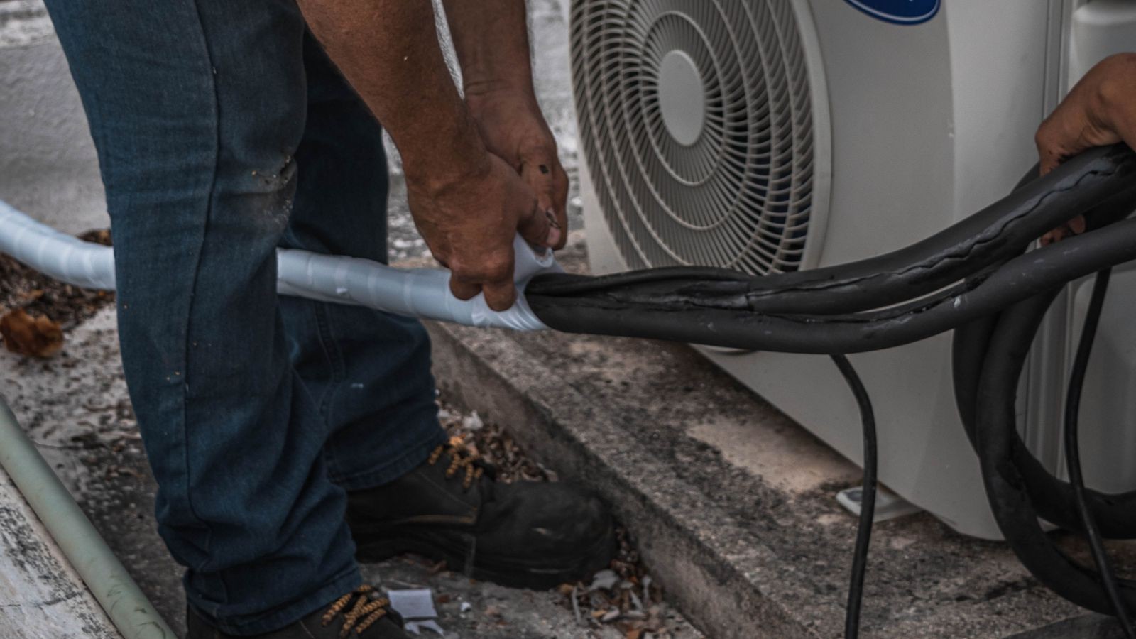 HVAC technician handling the drain and refrigerant lines at an outdoor air conditioning unit