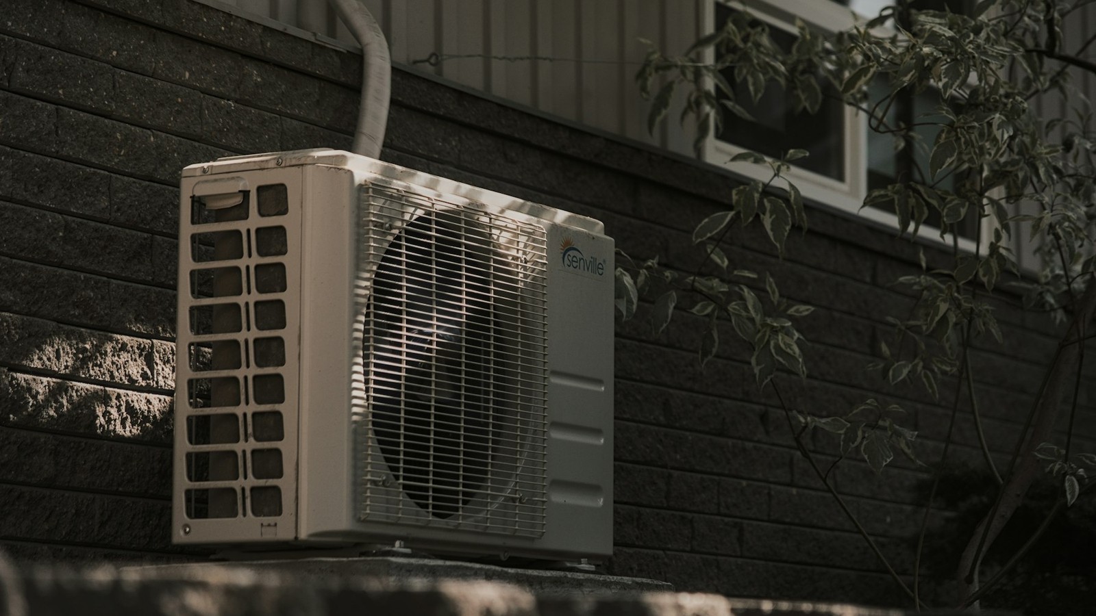 Outdoor air conditioning condenser mounted beside a home with its refrigerant line set running up the exterior wall