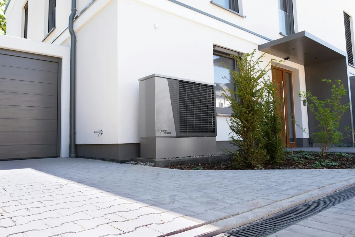 Modern outdoor heat pump / AC condenser unit installed beside a home's driveway and front entrance