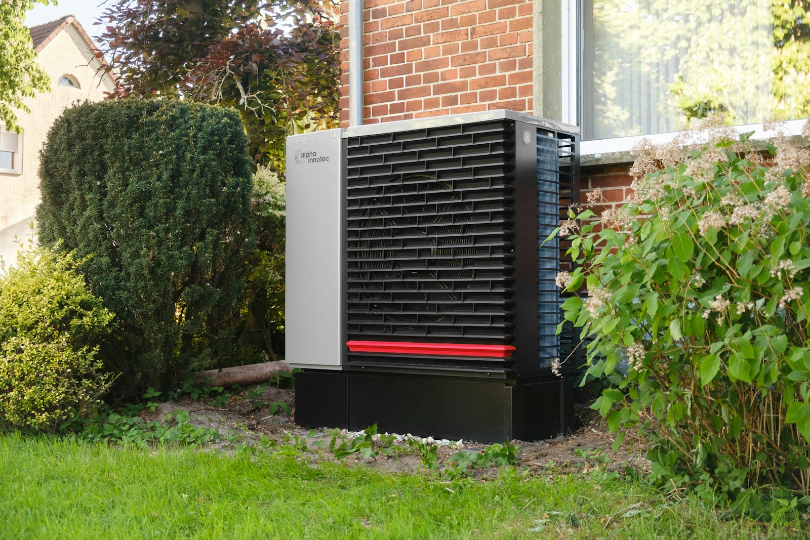 Outdoor heat pump AC condenser unit installed beside a brick home exterior