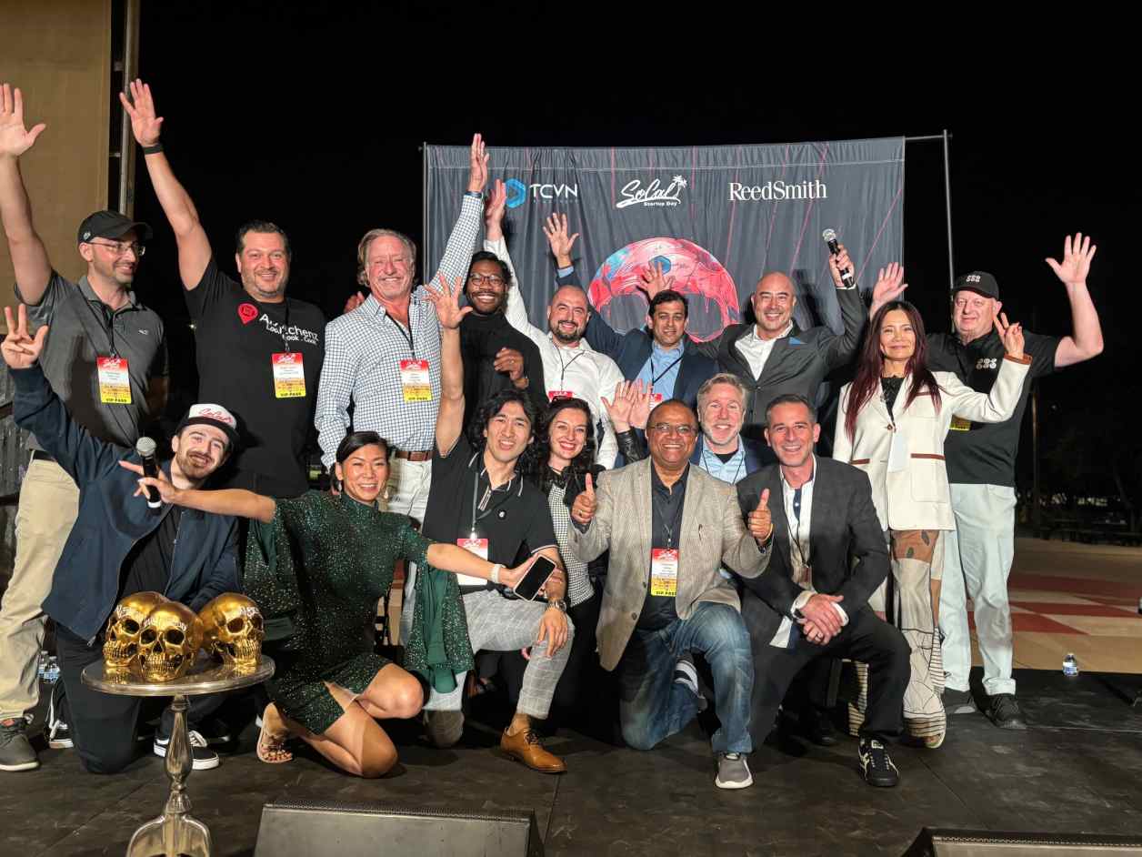 TCVN Survivor XII finalists, judges, and organizers celebrating on stage at night with TCVN, SoCal Startup Day, and ReedSmith banners in the background