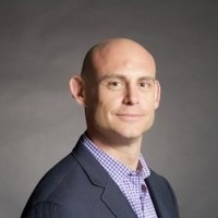 Professional headshot of a TCVN member or speaker in a suit against a gray background