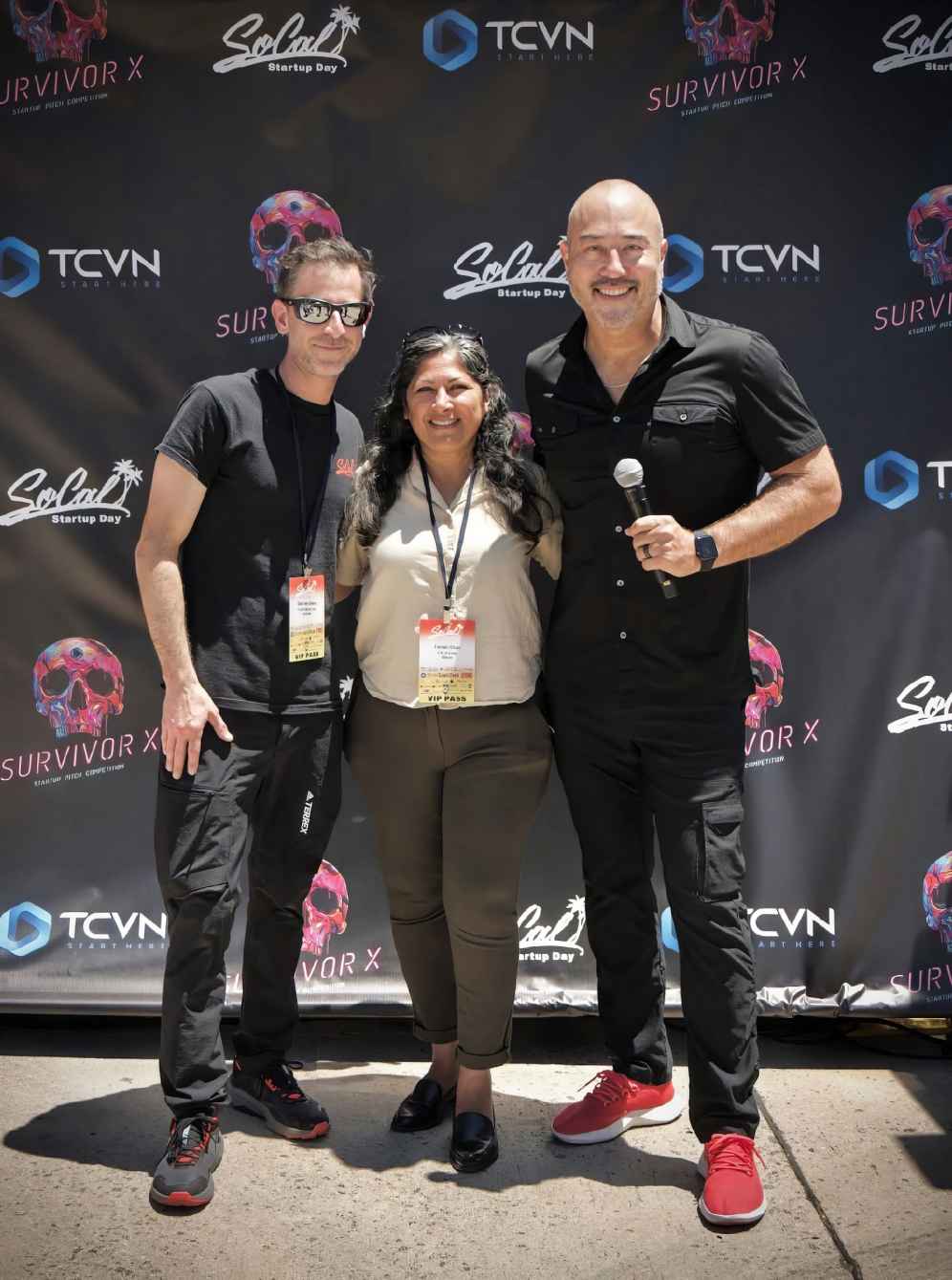 Three attendees posing together in front of the TCVN Survivor X Startup Pitch Competition step-and-repeat banner at SoCal Startup Day
